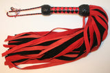 Leather Flogger made from red and black suede leather with a woven diamond pattern handle that has two black turks heads, one turks head on each end. 