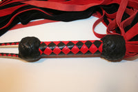 Leather Flogger made from red and black suede leather with a woven diamond pattern handle that has two black turks heads, one turks head on each end.  Handle detail closeup